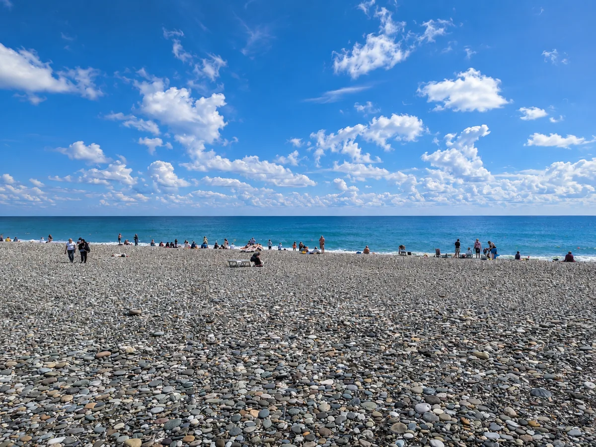 People relaxing on Batumi's pebble beach beside the Black Sea under a bright, partly cloudy sky, Adjara, Georgia