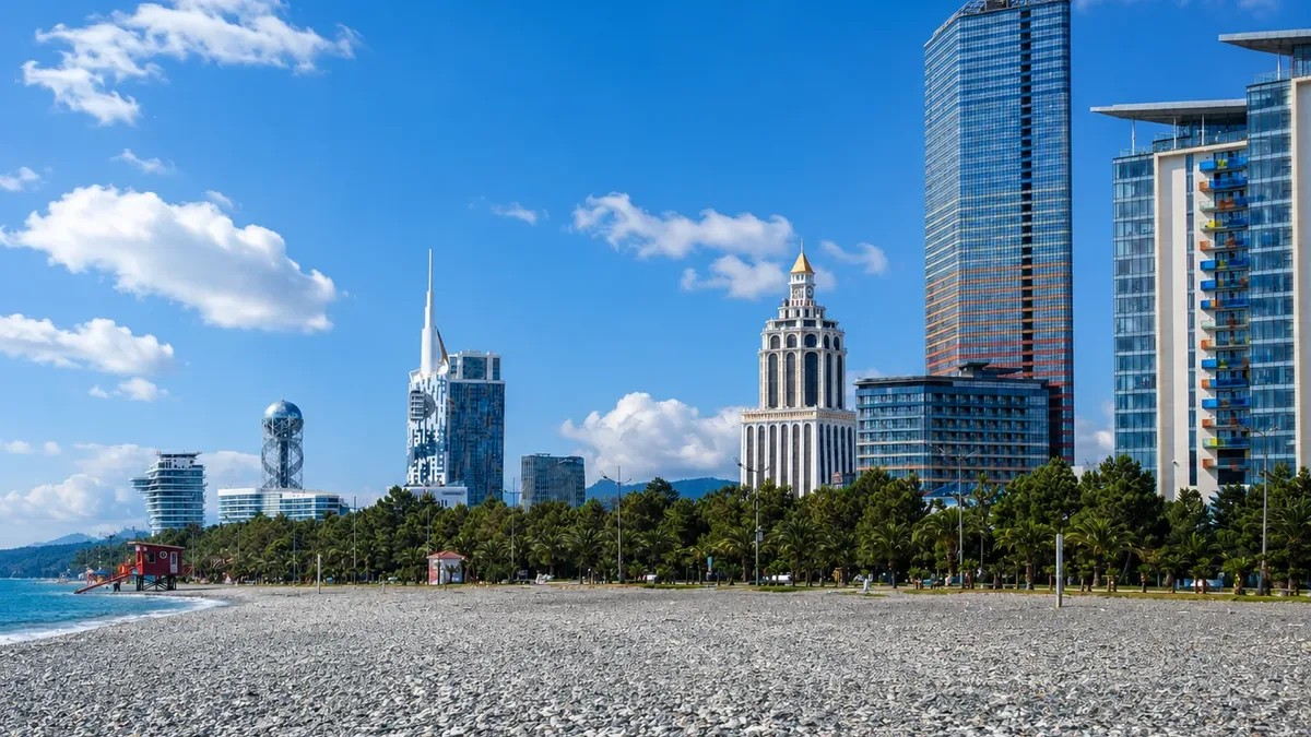 Moderní panoráma pobřeží Batumi s výškovými věžemi, včetně Alphabet Tower zakončené koulí, při pohledu přes oblázkovou pláž pod modrou oblohou, Adžárie, Gruzie