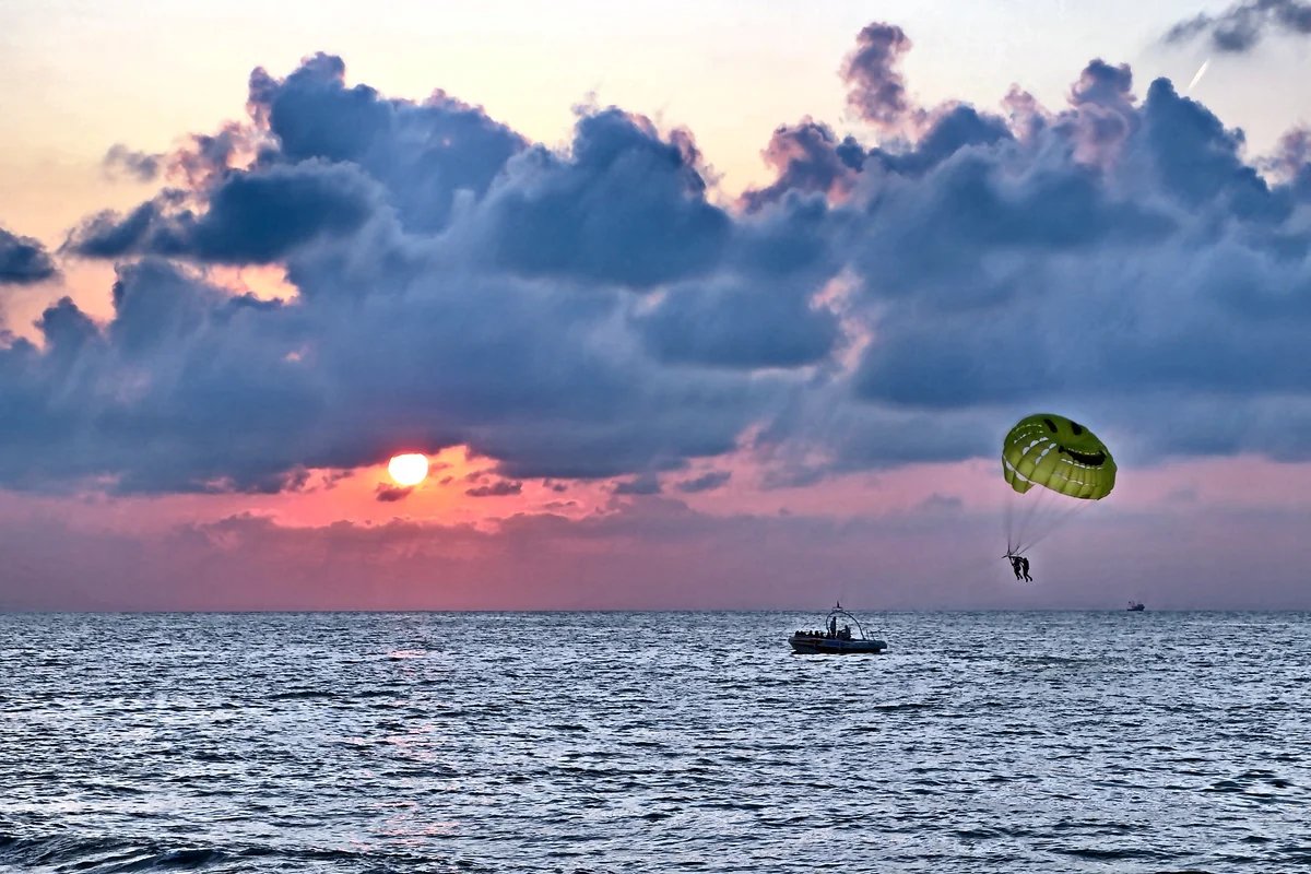 Parasailing over the Black Sea at sunset off Batumi, a boat towing a parachute against a pink and purple sky, Georgia