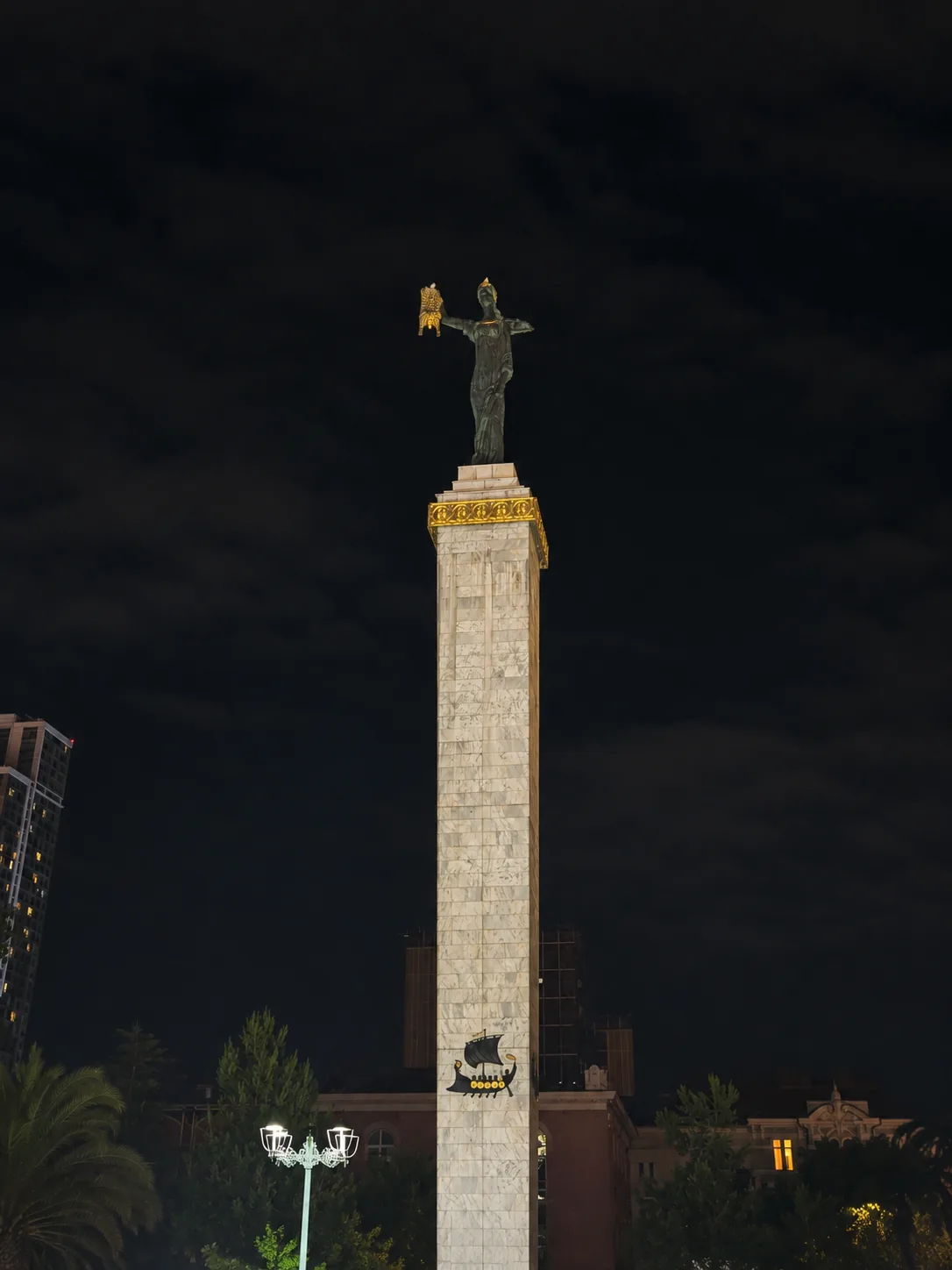 Brązowy posąg Medei trzymającej złote runo na szczycie wysokiej kolumny na placu Europy w Batumi, Gruzja, nocą
