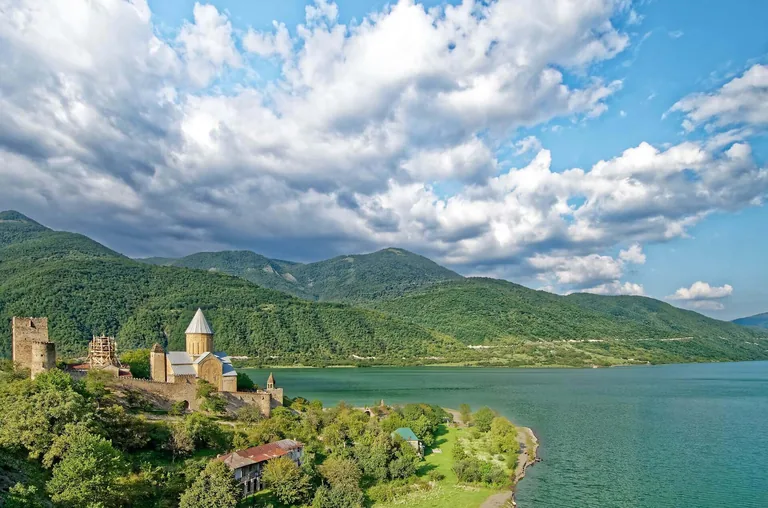 The Ananuri fortress and its domed church on a green hillside above the turquoise Zhinvali reservoir, backed by forested mountains, Georgia
