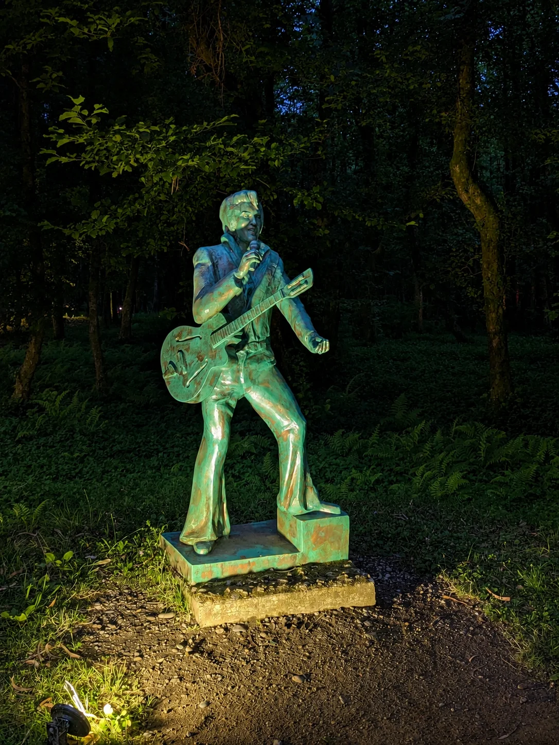 Una estatua de bronce de Elvis Presley con guitarra y micrófono, iluminada de noche en el Parque de los Músicos de Shekvetili, Georgia