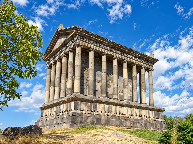 The Temple of Garni — a 1st-century Greco-Roman colonnaded temple of dark basalt on a raised podium, under a blue sky with clouds, Kotayk, Armenia