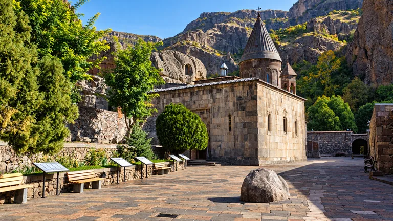 The UNESCO-listed Geghard Monastery — its medieval domed stone church in a paved courtyard below steep rocky cliffs, Upper Azat Valley, Armenia