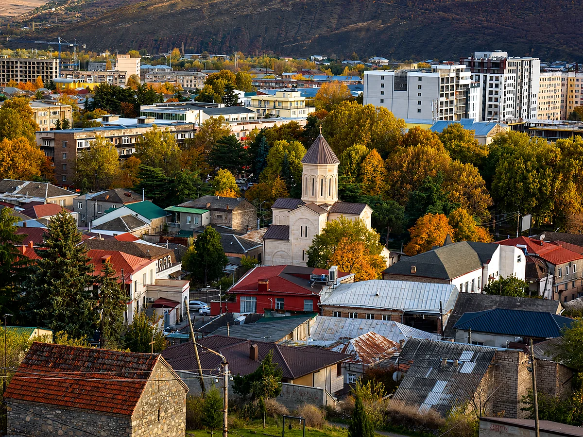 Una iglesia ortodoxa georgiana entre los tejados otoñales de Gori bajo las colinas circundantes, Shida Kartli, Georgia