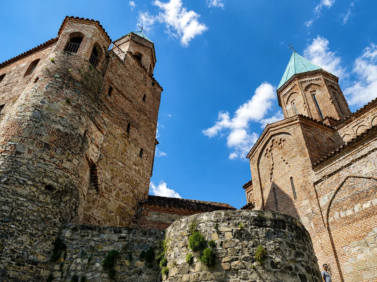 Zvonice a kostel Archandělů v Gremi při pohledu zdola, kamenné zdi a ozdobné cihlové zdivo proti modré obloze, Gruzie