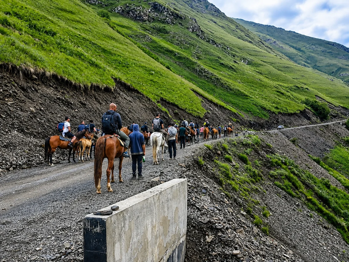 A horse-trekking group on a gravel mountain road in the green highlands of the Georgian Caucasus