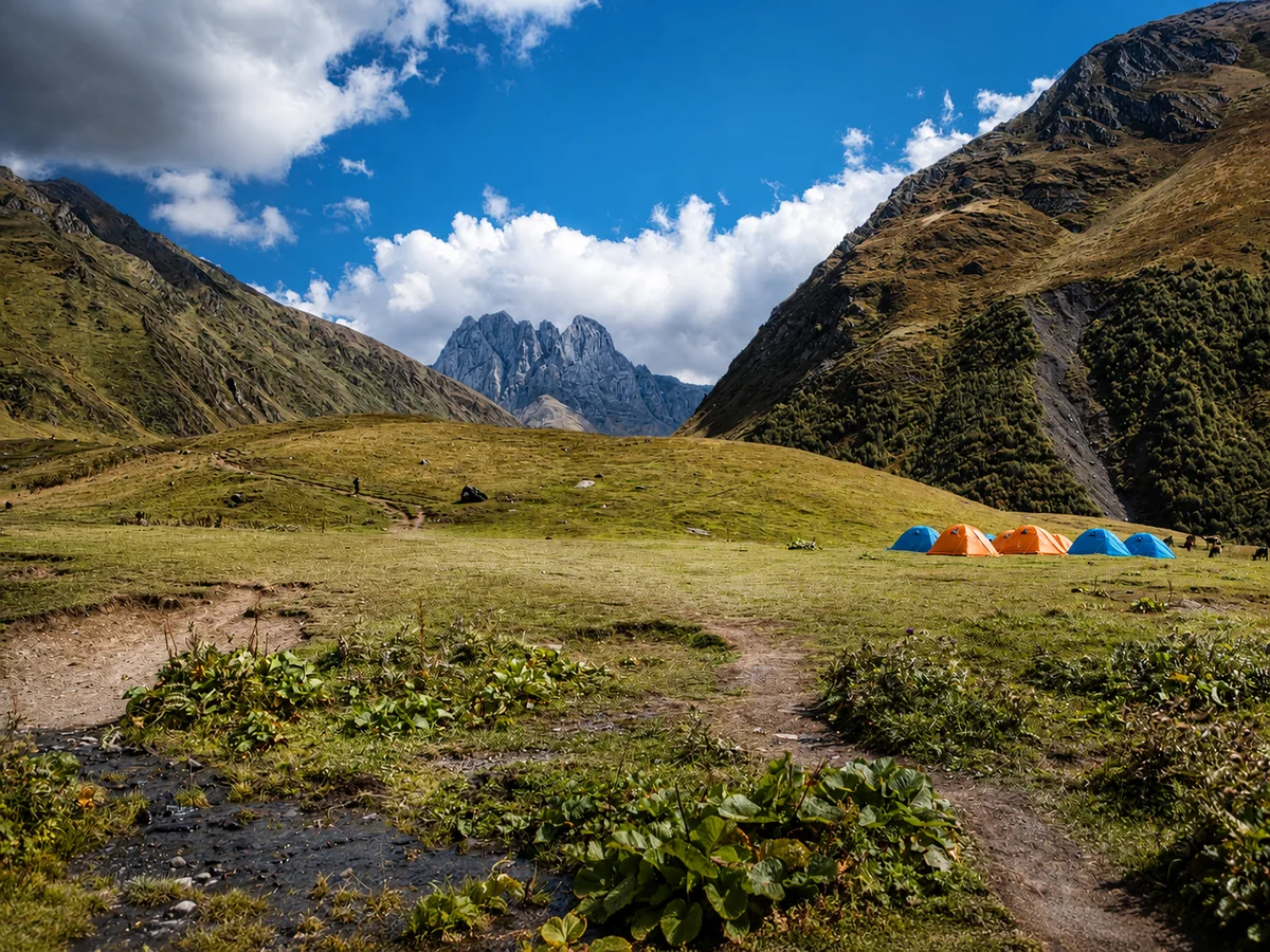Namioty trekkingowe na alpejskiej łące w dolinie Juty pod poszarpanymi szczytami Chaukhi, Kazbegi, Gruzja