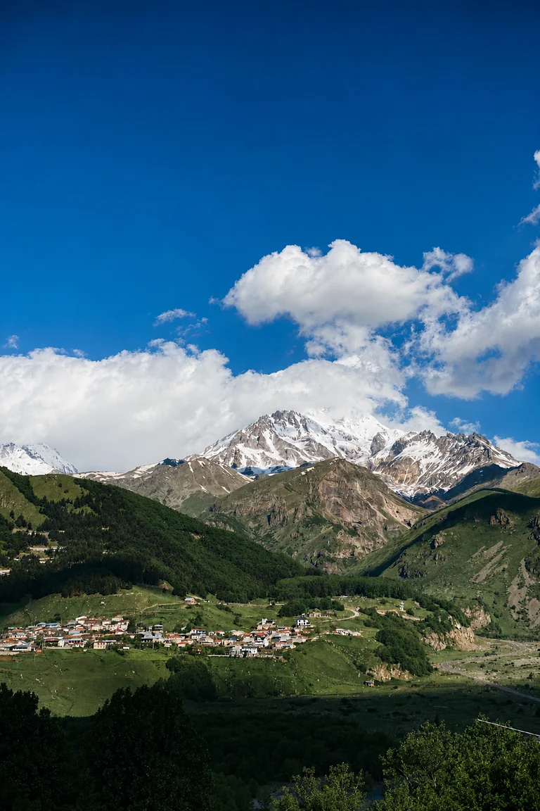Stepantsminda on its green slopes below a snow-capped Caucasus massif, Kazbegi, Georgia