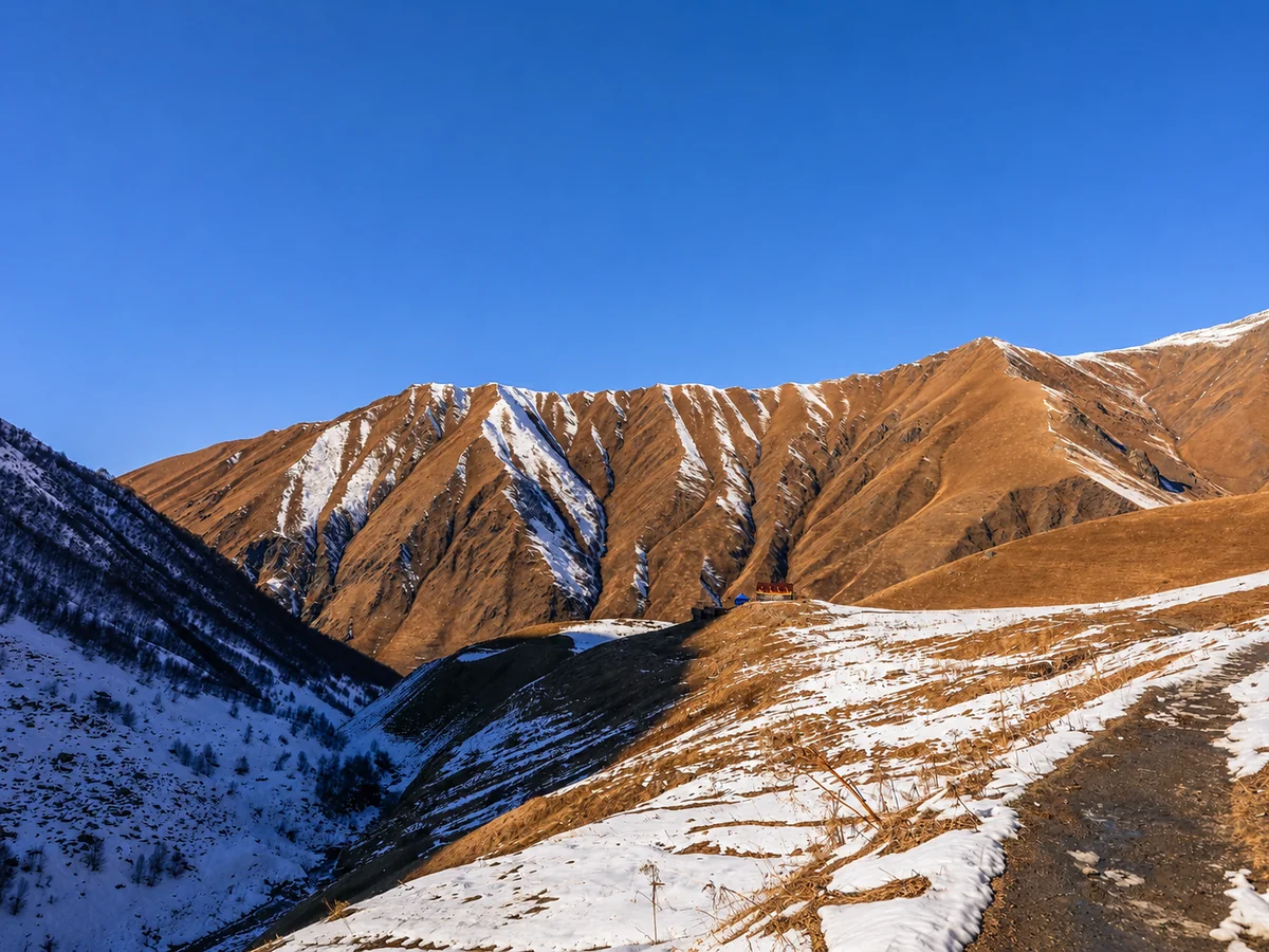 Brązowe grzbiety poprzecinane śniegiem nad doliną w górach Kazbegi zimą, Wielki Kaukaz, Gruzja