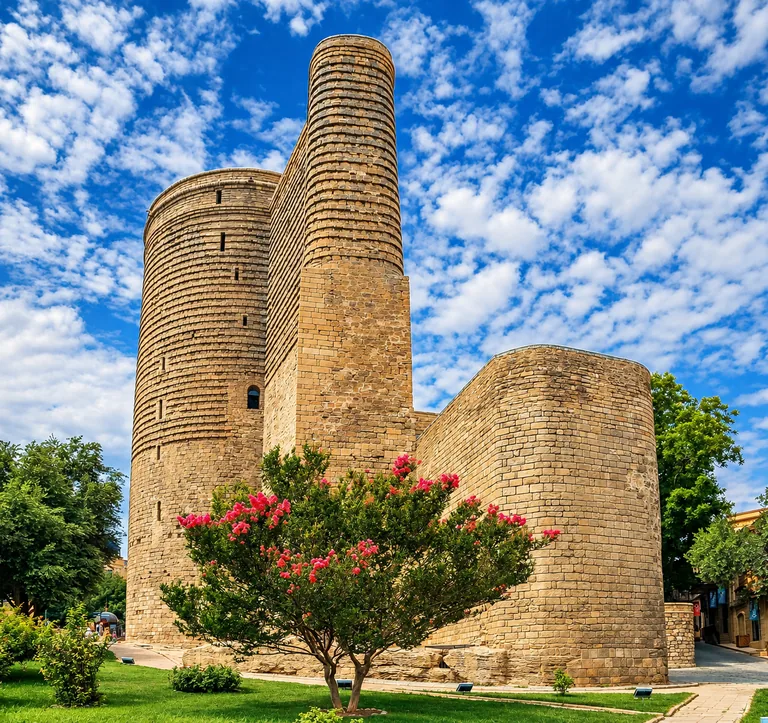 The medieval Maiden Tower in the UNESCO-listed Walled City of Baku, a tall cylindrical stone tower with a flowering tree in front, Azerbaijan