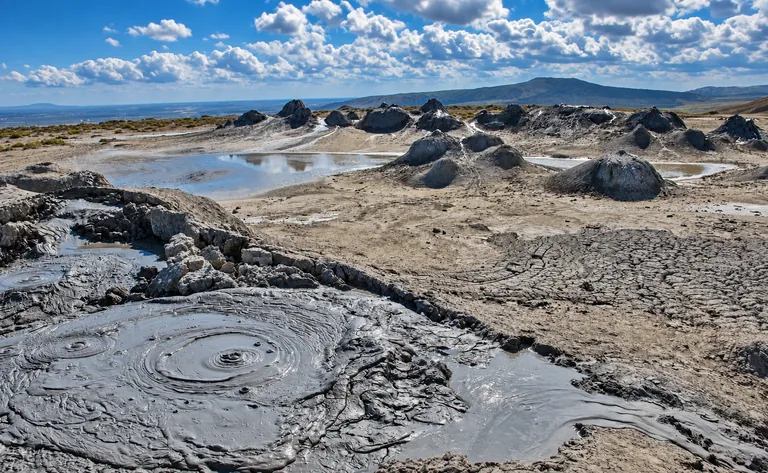 Cold grey mud bubbling from low cones at the mud volcanoes near Gobustan, on a bare semi-desert plain under a cloud-dotted sky, Azerbaijan
