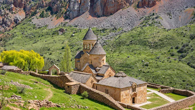 Klooster Noravank — de middeleeuwse goudkleurige stenen kerken met kegelkoepels, waaronder de tweelaagse Burtelashen, op een groene helling onder rood-grijze kalkstenen kliffen, Amaghu-kloof, Vajots Dzor, Armenië