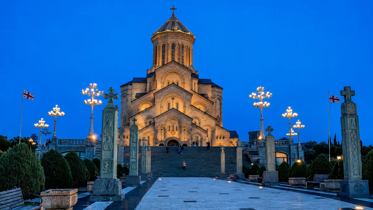 The floodlit Holy Trinity Cathedral of Tbilisi at blue hour, with its lamplit plaza and stone crosses, Georgia