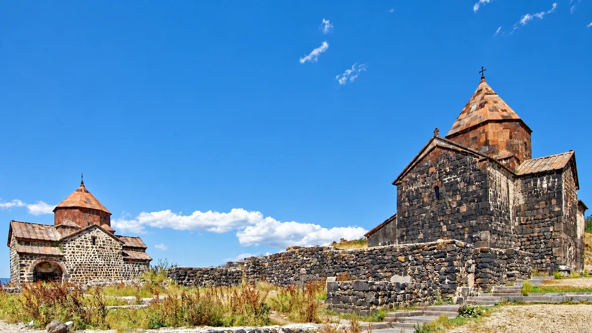 Two dark stone churches of Sevanavank Monastery with red-tiled conical domes under a blue sky, Armenia