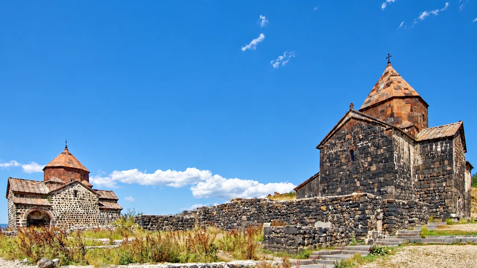 El monasterio de Sevanavank — sus dos iglesias del siglo IX de basalto oscuro con cúpulas cónicas de tejas en la península de Seván sobre el lago Seván bajo un cielo azul, Gegharkunik, Armenia