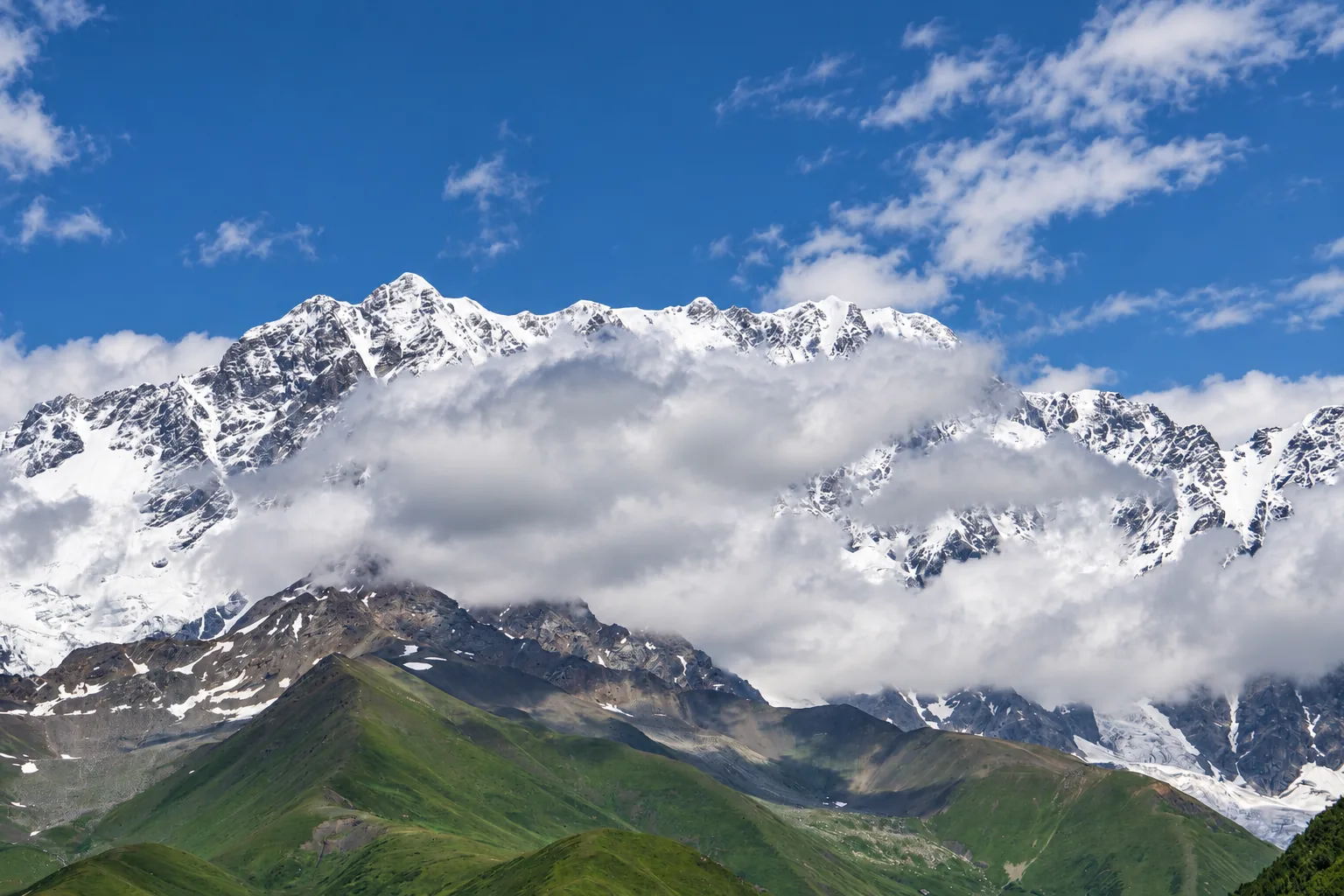 Schneebedeckte Gipfel des Schchara-Massivs im Hohen Kaukasus über grünen Vorbergen, Oberswanetien, Georgien