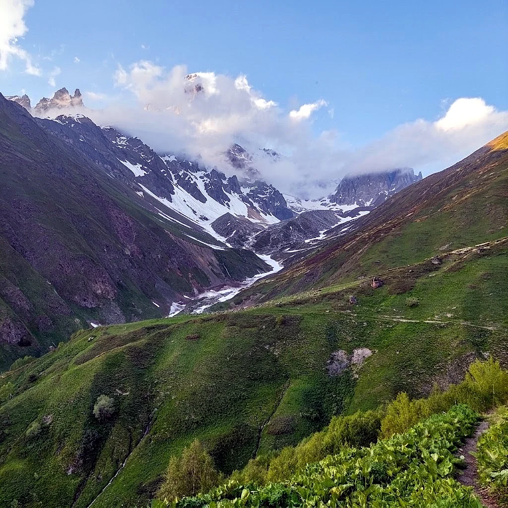 A glacier and snow-streaked peaks above a green alpine valley in Svaneti, Georgia