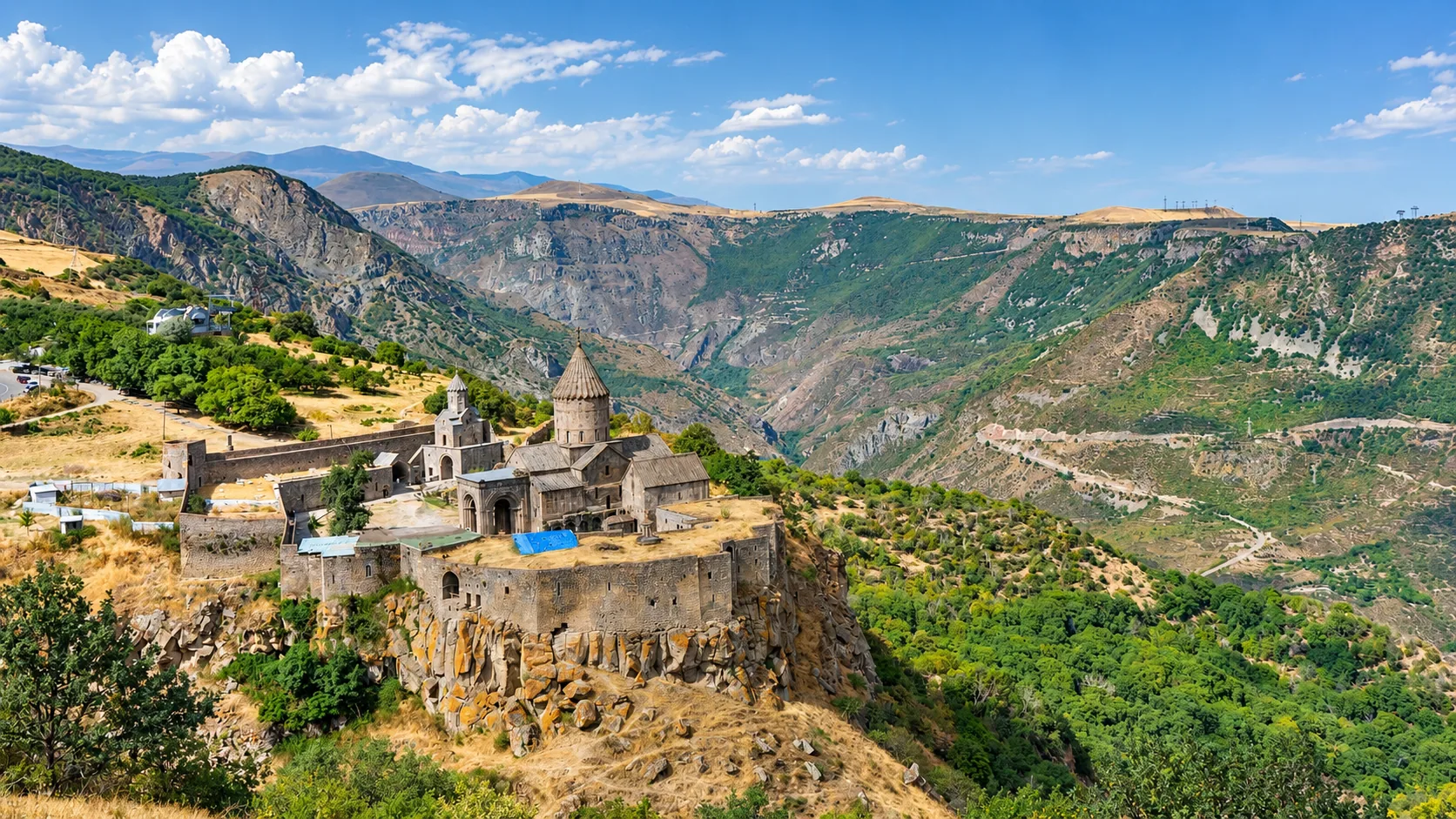 Klooster Tatev — een versterkt middeleeuws complex met een koepelkerk van donkere steen op een plateau boven de diepe Vorotan-kloof, omringd door bergen onder een blauwe hemel, Syunik, Armenië