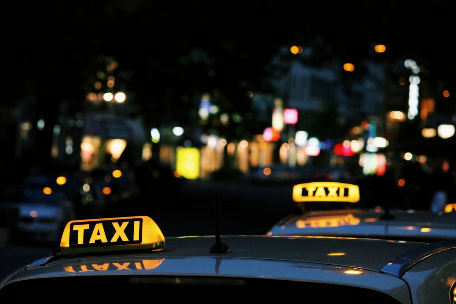Verlichte taxiborden op autodaken langs een stadsstraat bij nacht, shuttle- en transferservice in Georgië