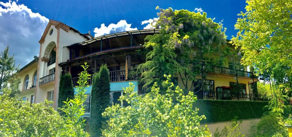 Buitenaanzicht met balkons tussen bomen en klimplanten, Casanova Inn in Dilijan, Armenië