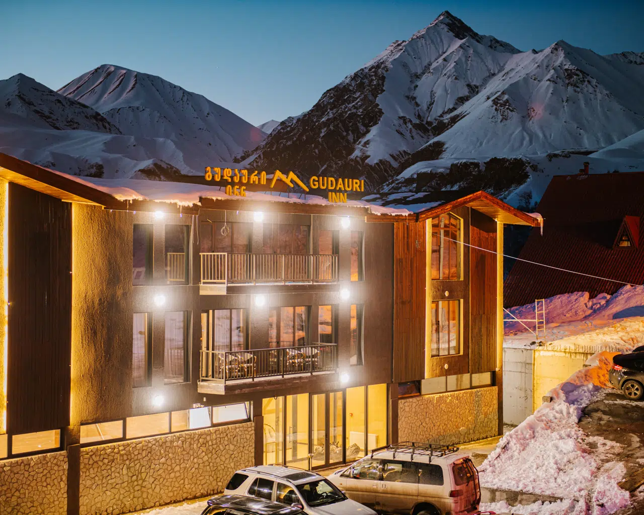 Außenansicht des Gudauri Inn in der Abenddämmerung unterhalb der verschneiten Gipfel in Gudauri, Georgien