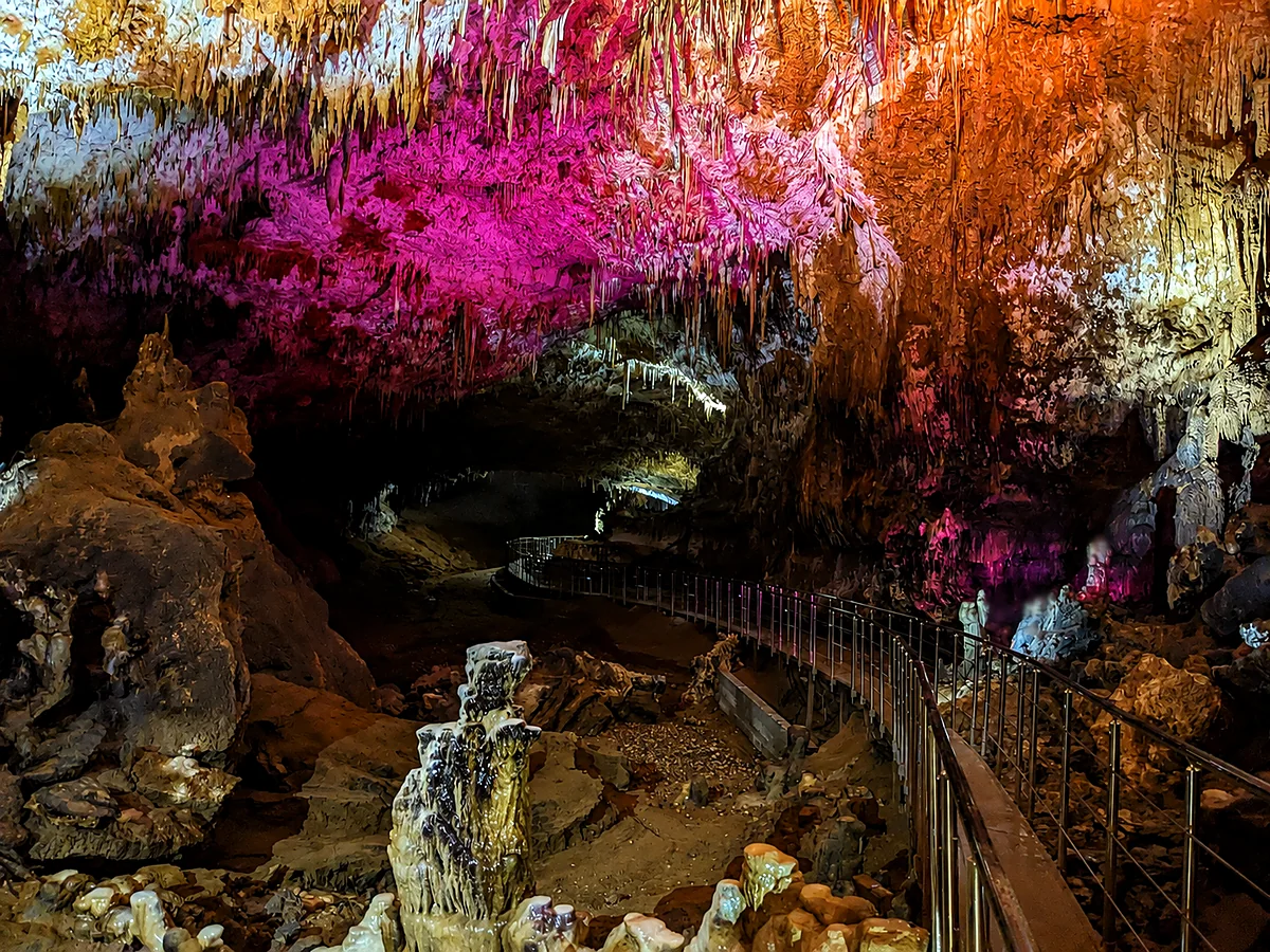 A lit cave hall with stalactites and a railed walkway at Prometheus Cave, Imereti, Georgia